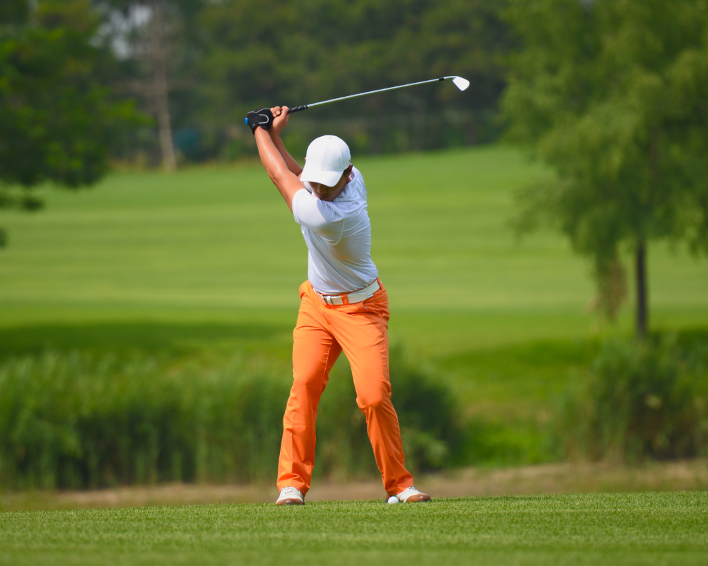 Golfer in white cap and orange pants ready to swing.
