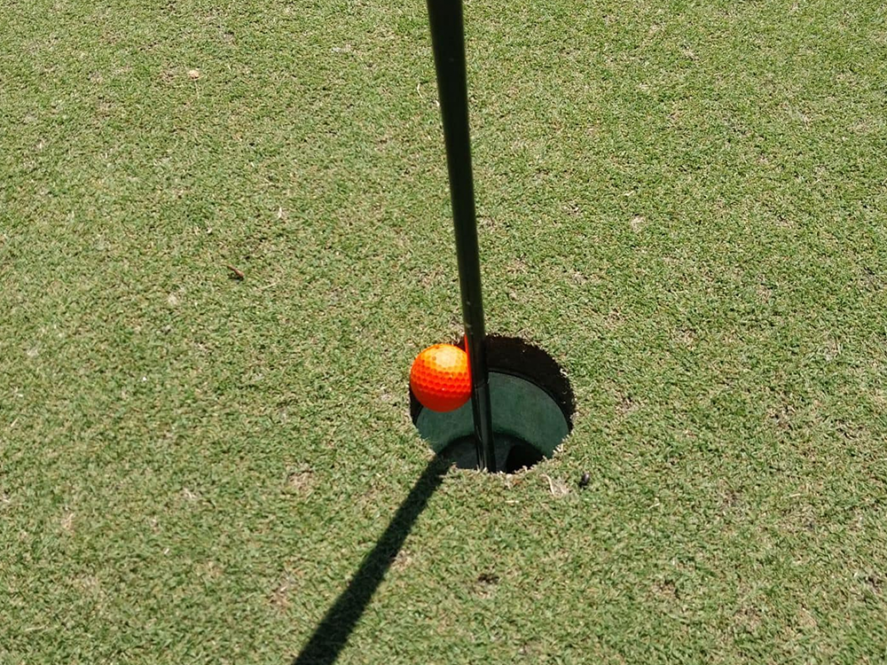 Neon golf ball hovering above hole